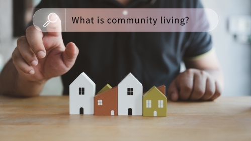 a person tapping on a search bar reading "what is community living?" at a table with toy houses