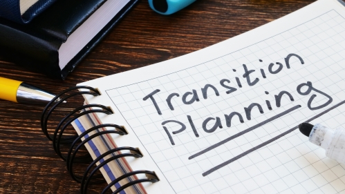 "Transition planning" written in marker and underlined on a notebook on a crowded desk