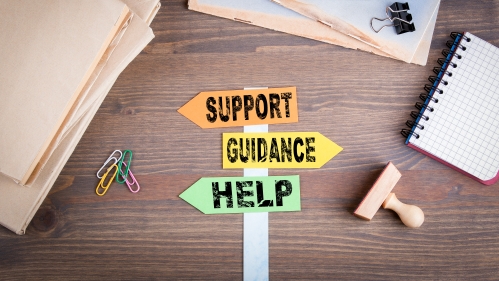 signpost cut-outs reading "support" "guidance" and "help" on a table with office supplies