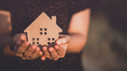 two hands cradling a wooden silhouette of a house