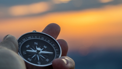 fingers holding a compass set against a blurred sky