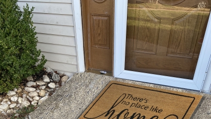sidewalk leading up to the front door of a home with a welcome mat reading "there's no place like home"