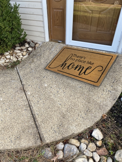 sidewalk leading up to the front door of a home with a welcome mat reading "there's no place like home"